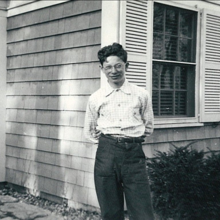Sam Harris, 1948, smiling child wearing glasses standing in front of a house