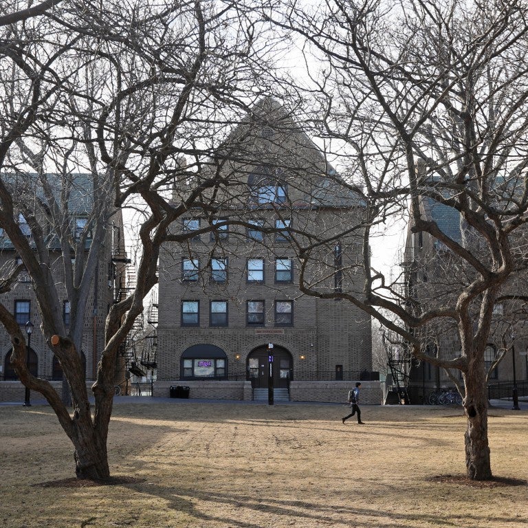 image of Northwestern University campus with bare trees, three light brown brick buildings, one person walking across a bare lawn.