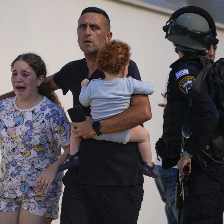 four figures, left to right: one young girl, crying. man with his arm around her, holding a small child. police officer guiding them.